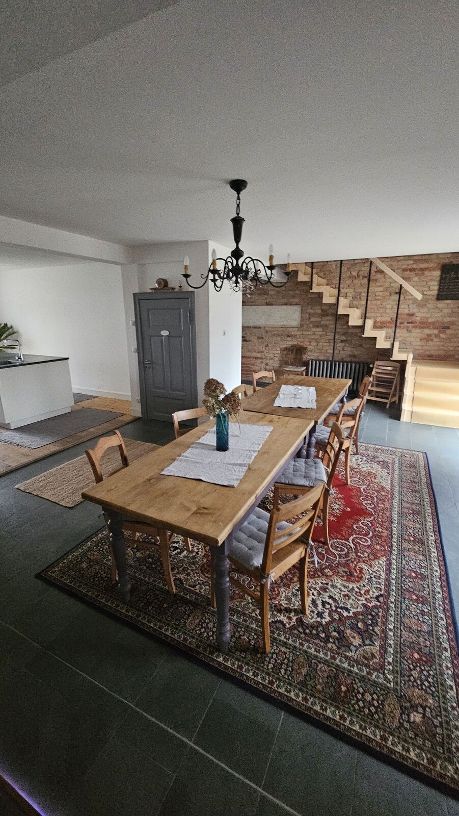 Fertiger Wohnraum mit langem Holztisch, Teppich und offener Treppe
