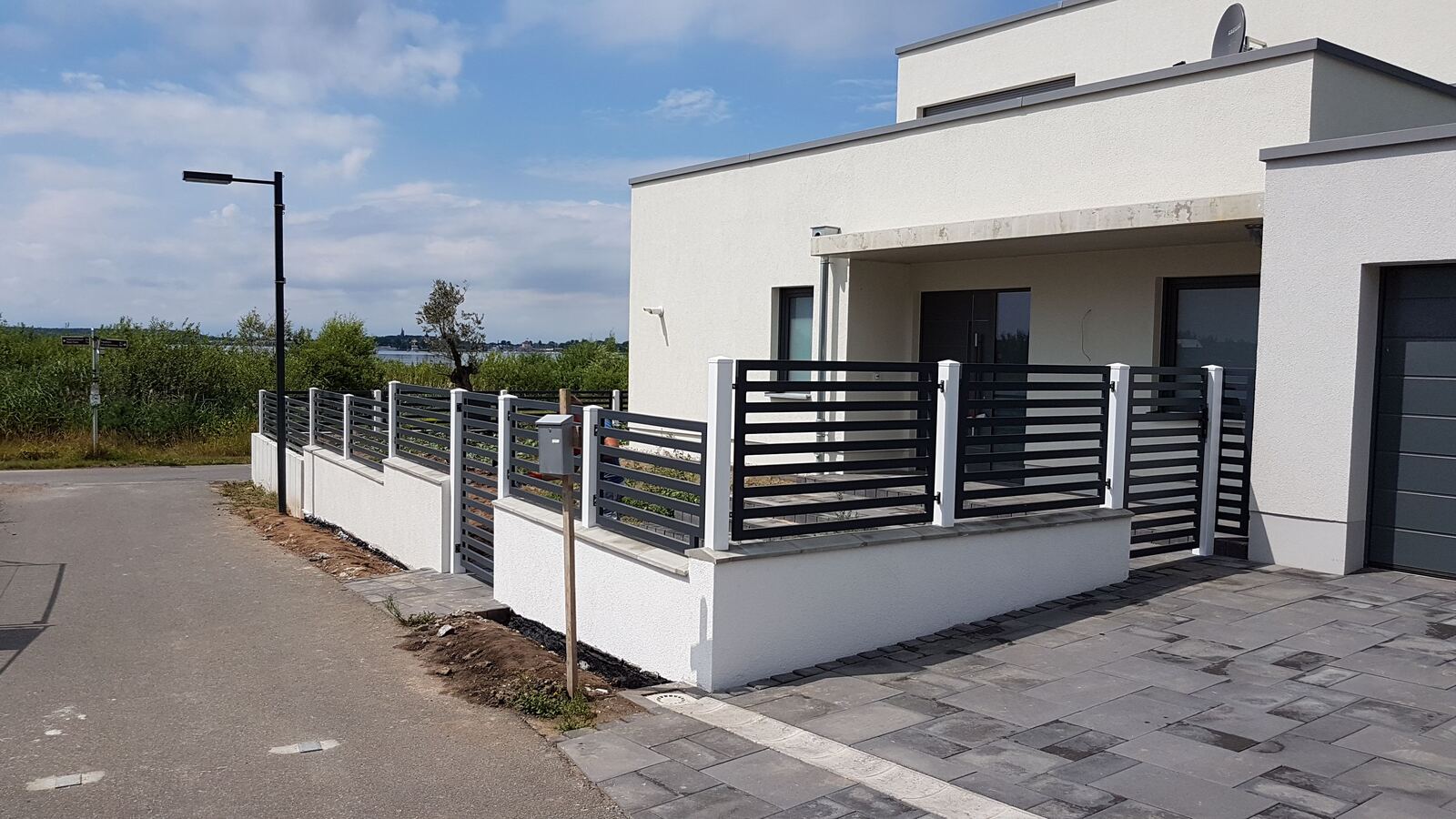 Fertige Einfriedung mit Betonsockel und Metallzaun vor einem weißen Haus